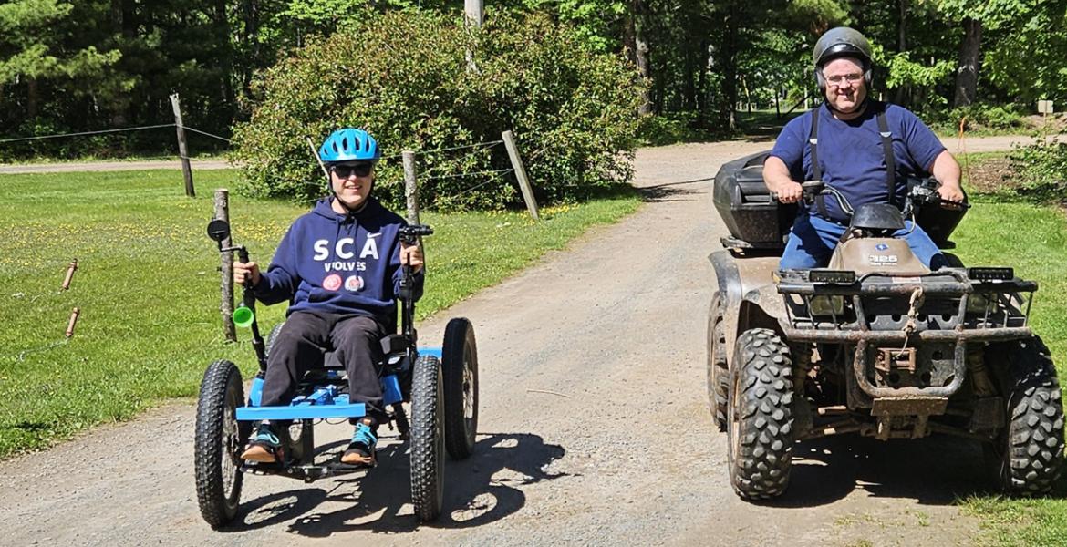Teenage boy on blue all-terain rig and helmet beside his dad on a four-wheeler
