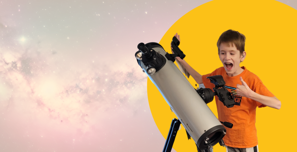 Young boy standing in excitement wearing an orange shirt behind a telescope