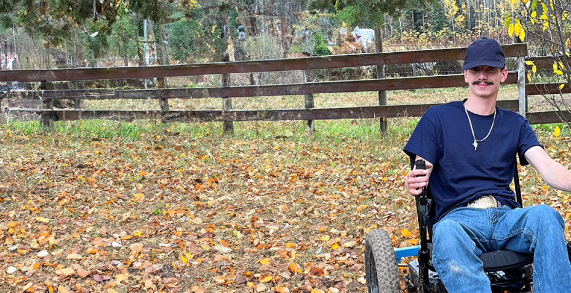 Ty in his all-terrain rig outside on his family farm with fall leaves, a tree, and fence